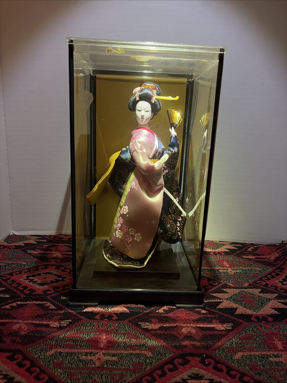 A vintage Japanese geisha doll in a glass display case.