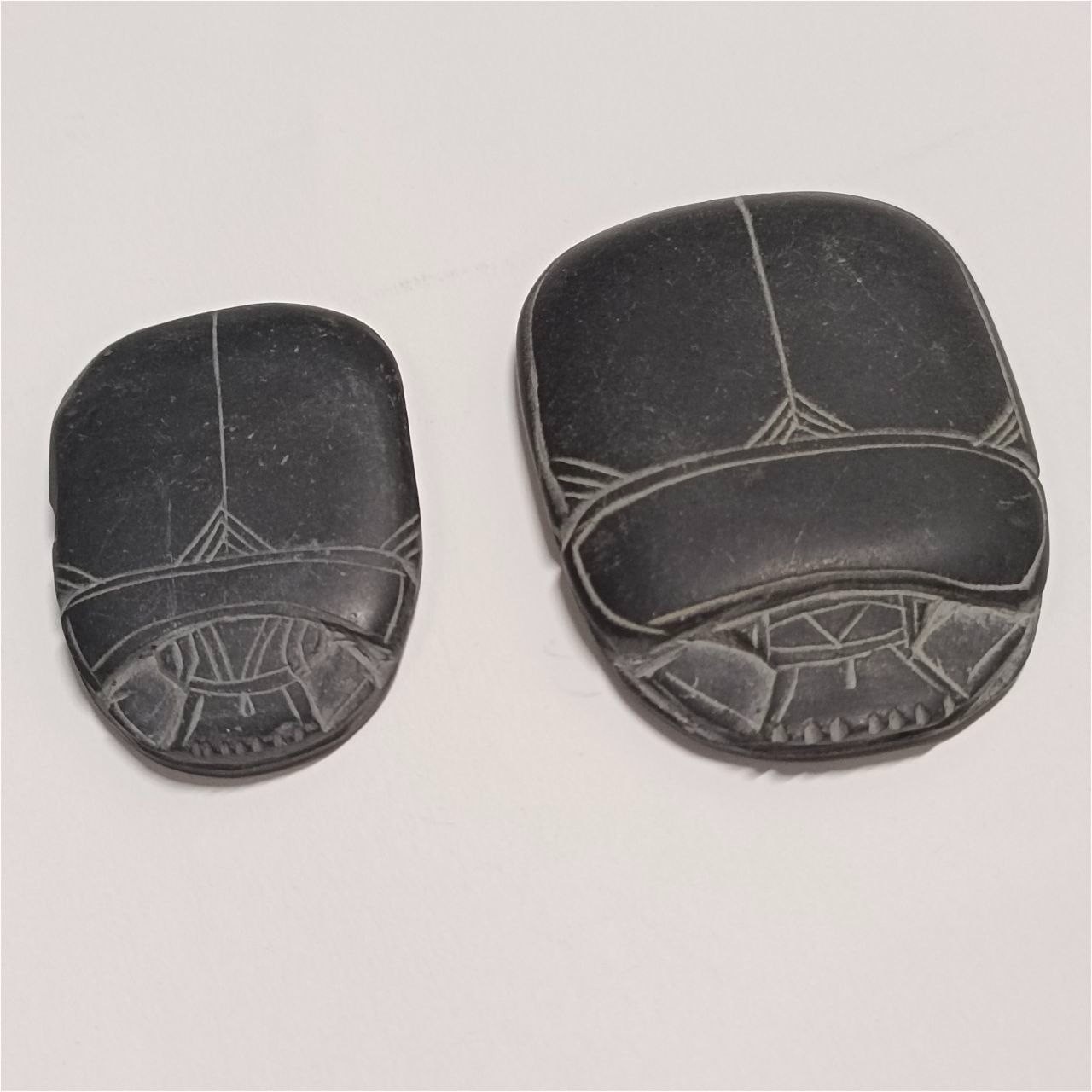 Two black carved stones with geometric patterns, handcrafted scarab design.
