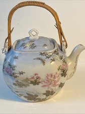 an antique porcelain teapot with hand-painted floral motifs and a woven handle. picture