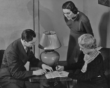 Woman signing a document as a man and woman look on circa 1940's Old Photo picture